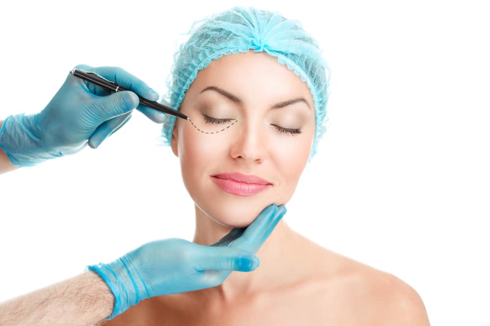 Woman, wearing a cap before surgery, closes eyes as her doctor plans her facelift