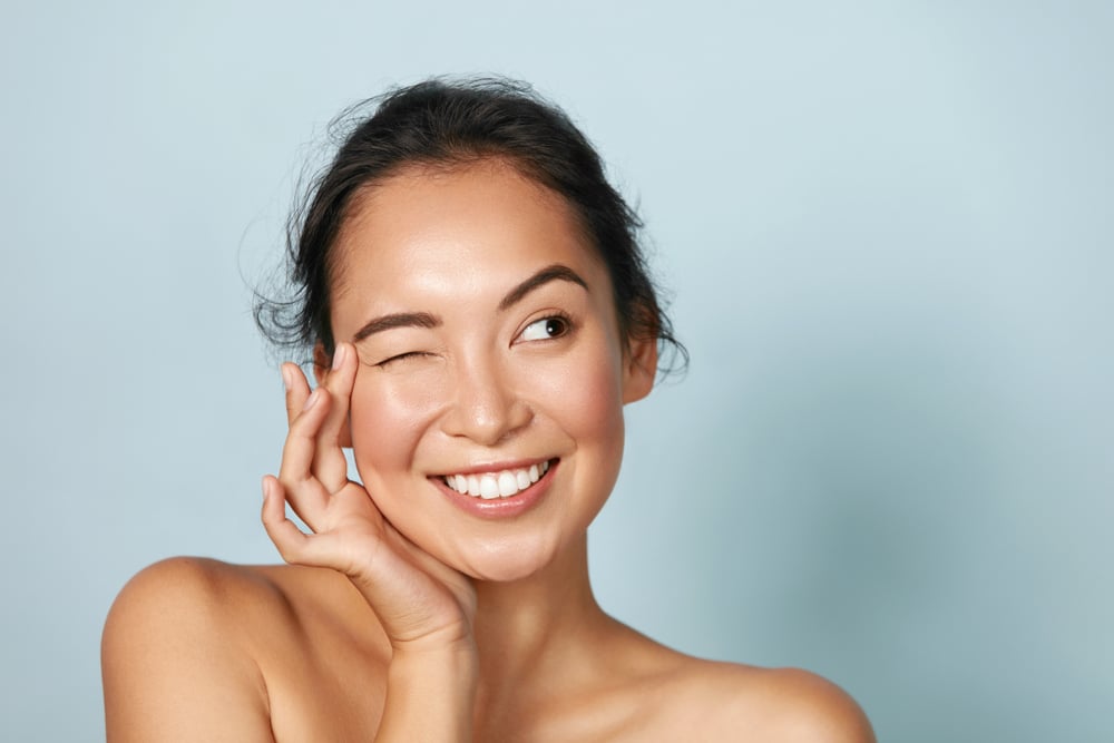 Woman smiles, winking and looking to the side, feeling confident thanks to her new skincare plan