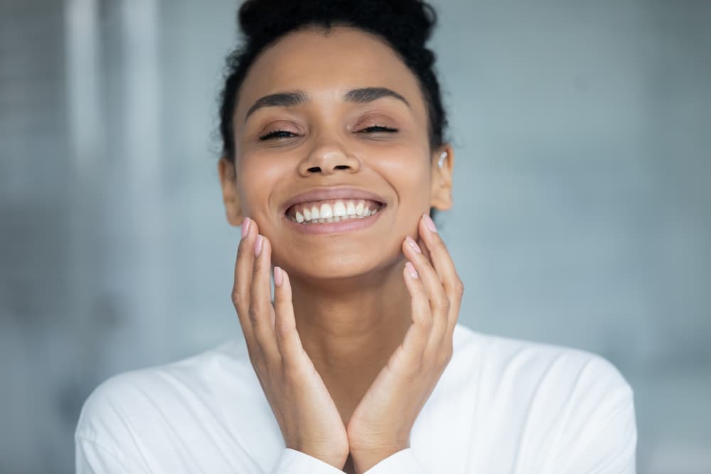 Beautiful woman jubilantly holds her face in her hands after a skin rejuvenation treatment