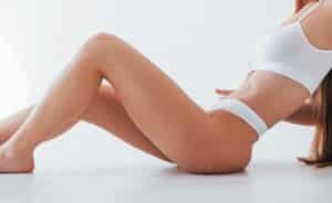 Woman wearing white underwear sits on the floor, revealing a slim, sculpted figure after liposuction before 2026